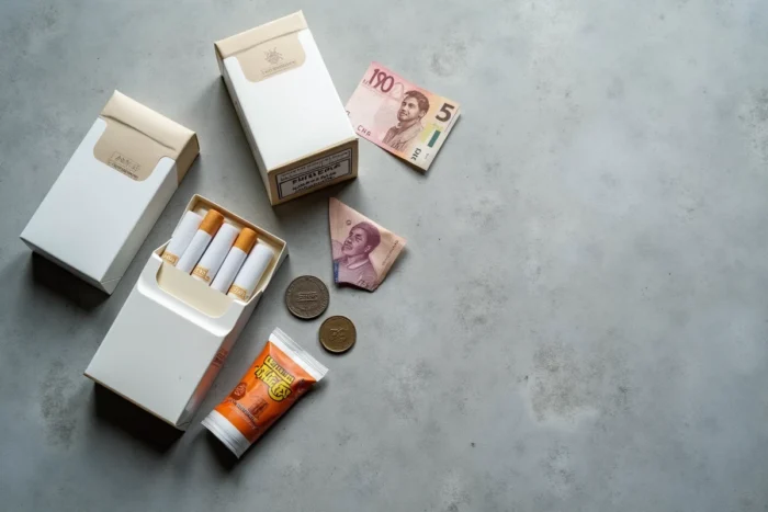 Paquets de cigarettes et monnaie suisse disposés sur béton pour comparer les prix du tabac en 2026